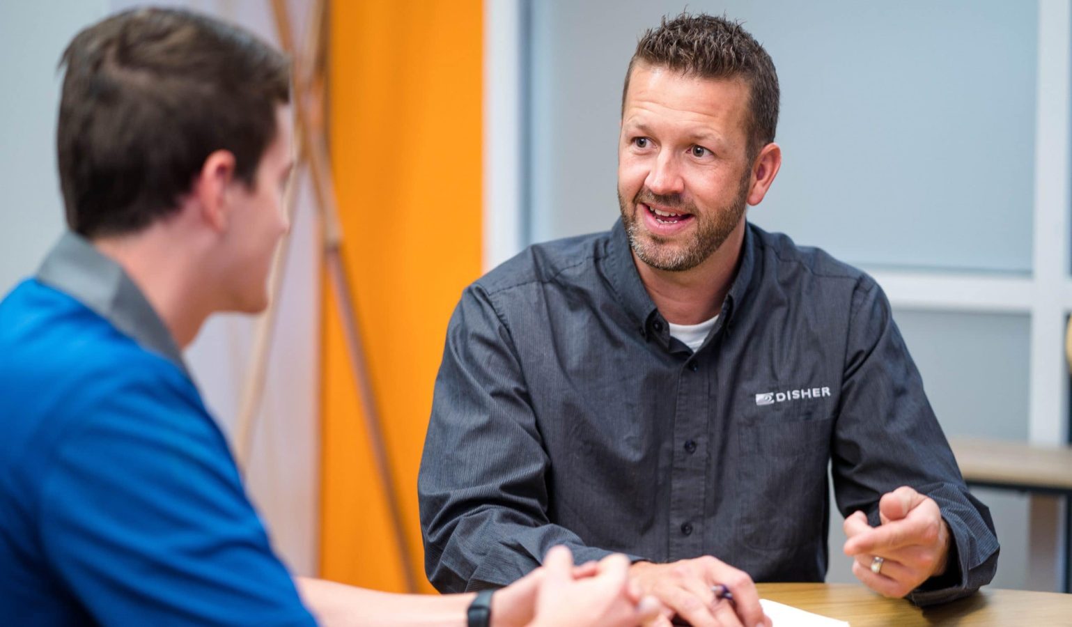 Senior male employee at DISHER sits with a junior male employee at DISHER to discuss mentorship.